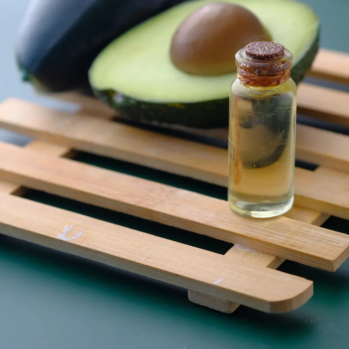 Avocado beside a small glass bottle of golden oil