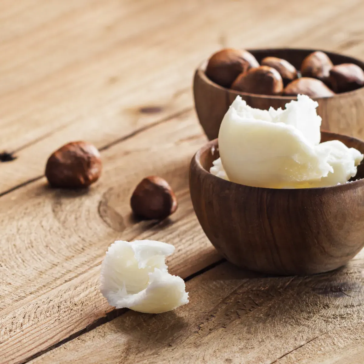 Shea nuts and pieces of unrefined shea butter in wooden bowls